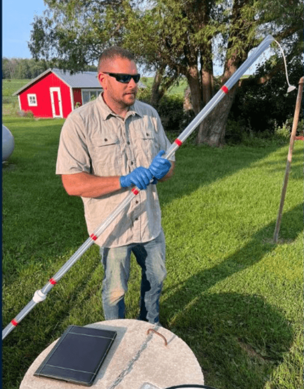 Technician in blue gloves holds a long sampling tube over a concrete well cover.